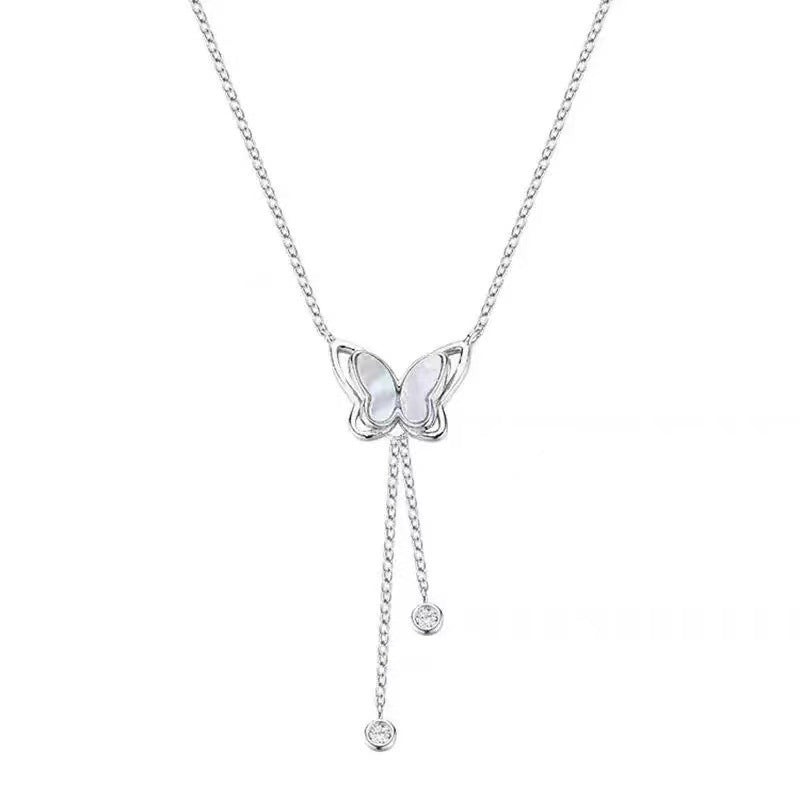 Close up of a silver tone butterfly necklace with white shell wings worn on a collarbone