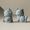 Two small gray stone cat figurines sitting side by side on a neutral surface
