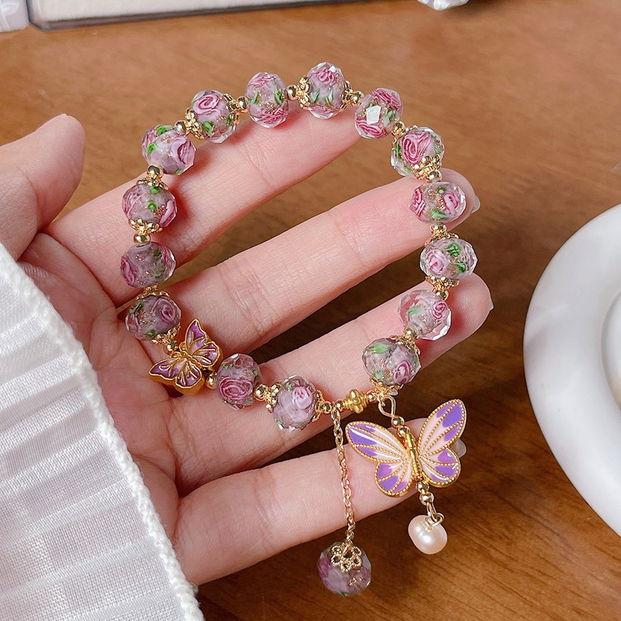 Pink floral glass bead bracelet with gold butterfly charm held in hand
