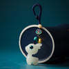 Close-up of a white glowing deer keychain with blue eyes and a gold-tone bell