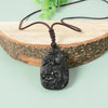 Close-up of a carved black obsidian pendant with dragon and phoenix designs on a brown cord