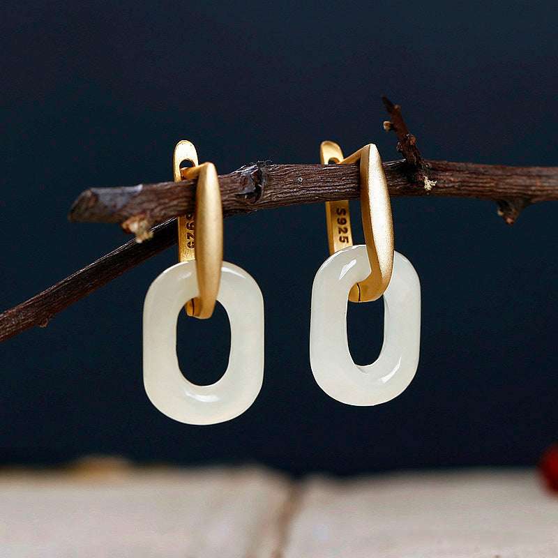 Pair of white jade geometric hoop earrings with gold tone accents hanging on a branch