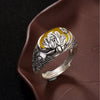 Close-up of a silver-tone adjustable ring with a yellow oval stone and engraved lotus flowers on the band.