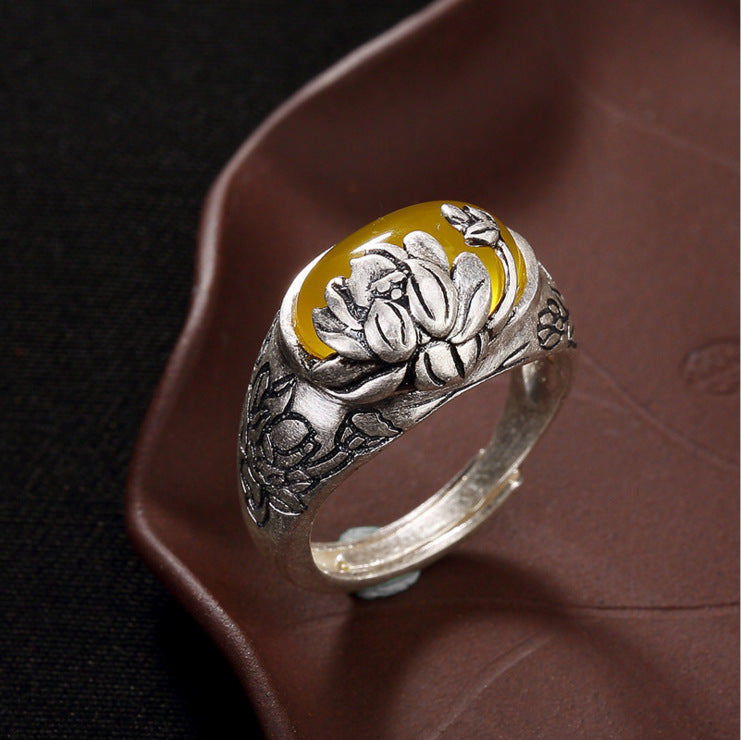 Close-up of a silver-tone adjustable ring with a yellow oval stone and engraved lotus flowers on the band.
