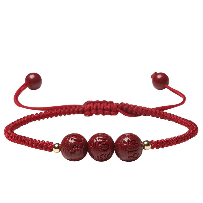 Three red cinnabar beads engraved with mantras on a braided red cord bracelet