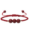 Three red cinnabar beads engraved with mantras on a braided red cord bracelet