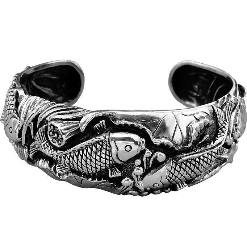 Silver tone open cuff bracelet with koi fish and lotus flower relief design on a wrist