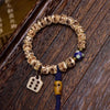 Close up view of a carved bone bead bracelet with a blue tassel and square charm on a wooden surface