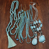 A collection of turquoise beaded necklaces with tassels and silver-tone pendants on wood