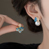 Close up of asymmetric stud earring with blue enamel flower and pearl