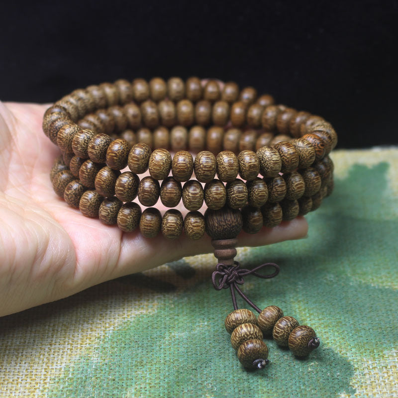 Close up of a hand holding a coiled 108 bead dark wood mala bracelet