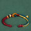 Close-up of a multi-colored woven rope bracelet with a mandala knot and leaf charm on a green background