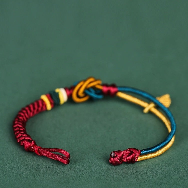 Close-up of a multi-colored woven rope bracelet with a mandala knot and leaf charm on a green background