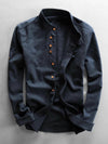 Dark blue men's long sleeve linen shirt with stand collar laid flat on a grey background