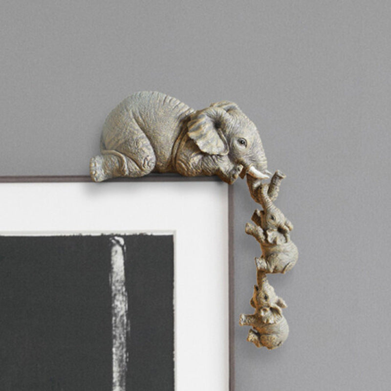 Three grey resin elephant figurines sitting on a white picture frame.