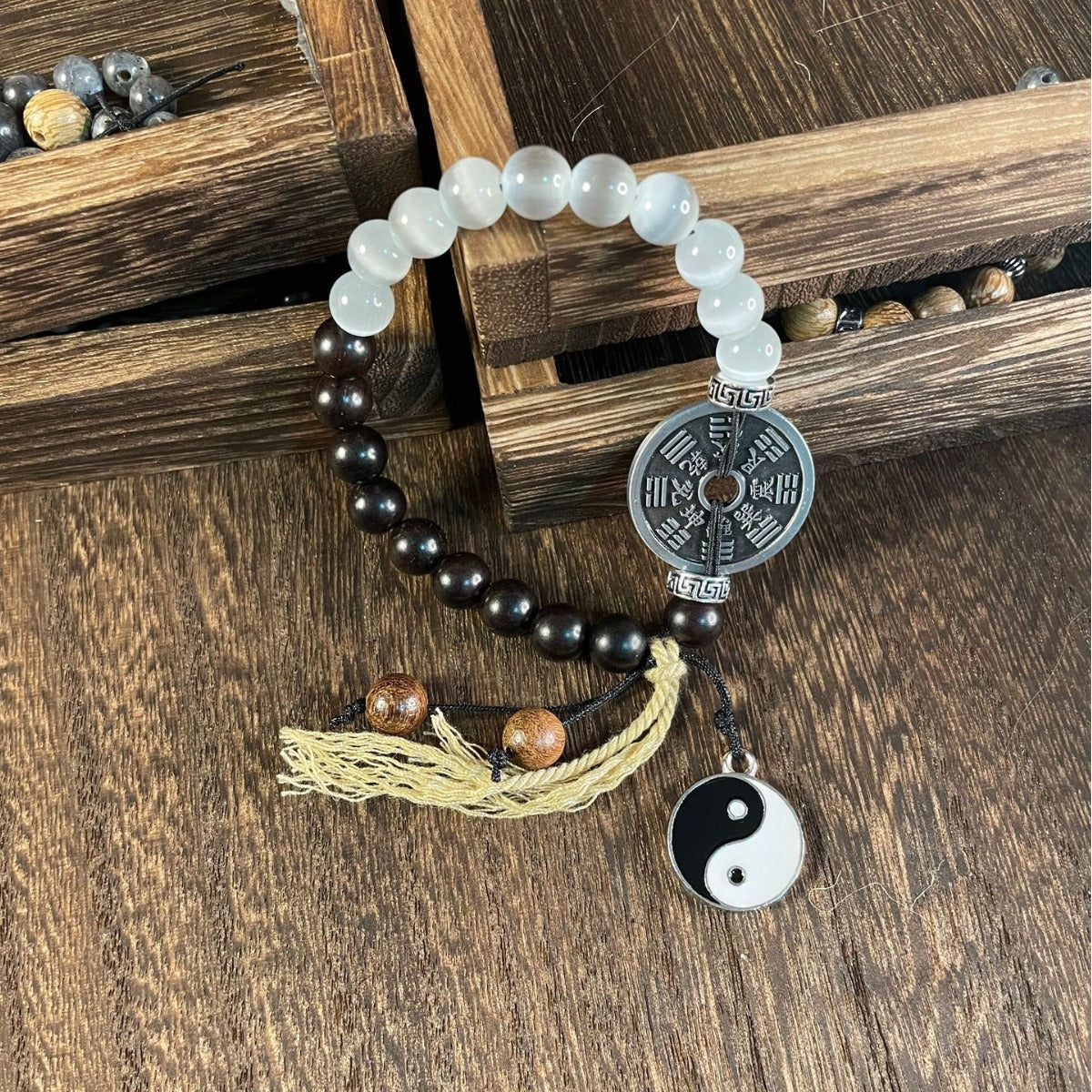 A bracelet with black and white beads, a metal coin charm, and a Yin Yang pendant resting on paper with calligraphy