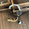 A bracelet with black and white beads, a metal coin charm, and a Yin Yang pendant resting on paper with calligraphy