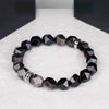 Faceted black silver obsidian bracelet with a silver-tone alloy charm on a white surface