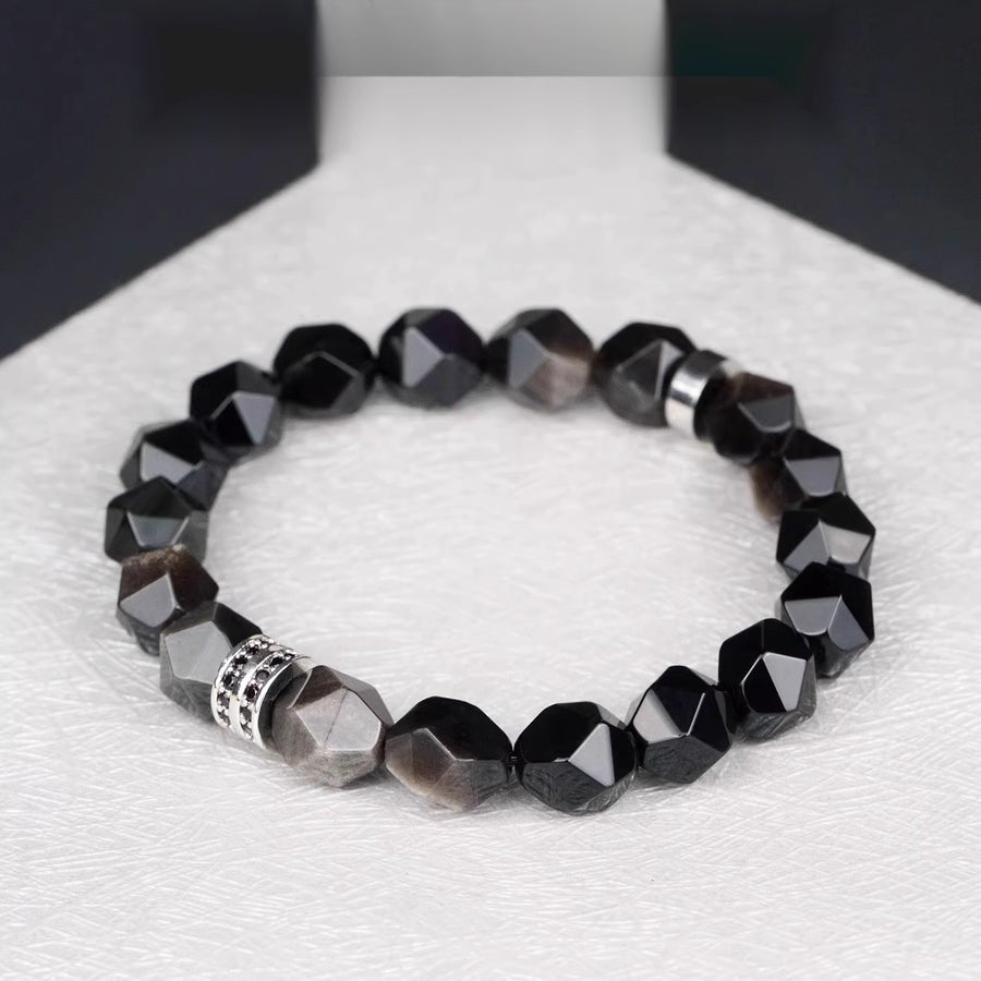 Faceted black silver obsidian bracelet with a silver-tone alloy charm on a white surface