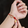 A wrist wearing a red braided bracelet with a white jade donut charm and a gold pendant.