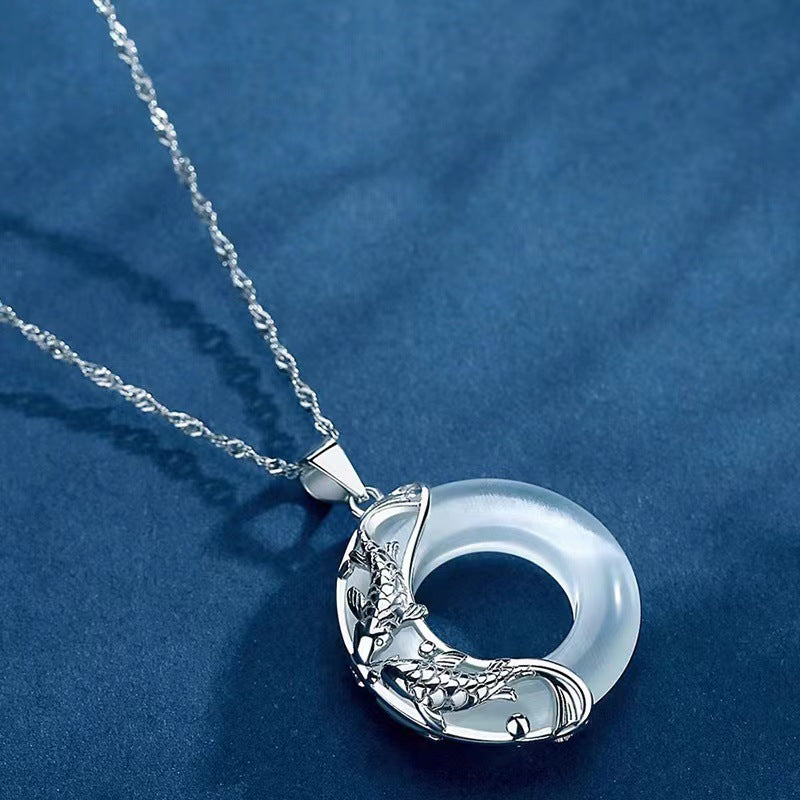 Close up of silver koi fish wrapping around a white jade peace buckle pendant on a blue background