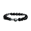 Close up of a black obsidian beaded bracelet with a silver geometric charm on a dark background.