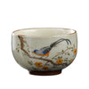 Close up of a cream colored ceramic tea cup with a blue bird painting