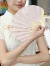 A woman holding a pale pink embroidered bamboo folding fan