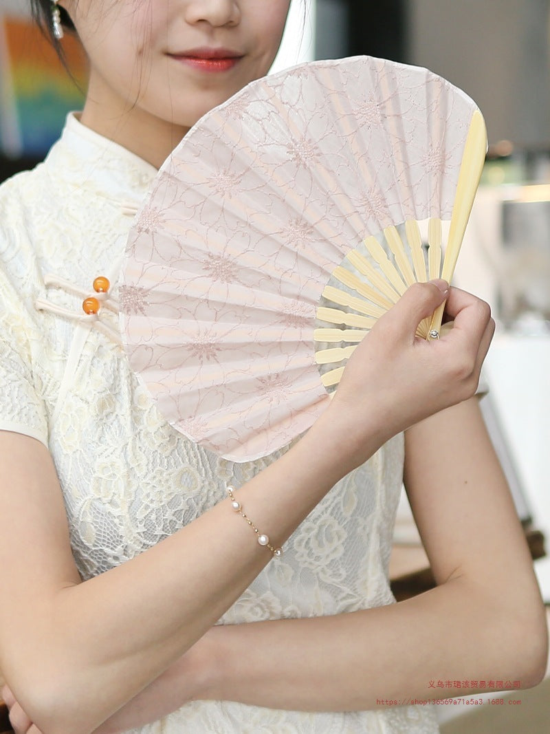 A woman holding a pale pink embroidered bamboo folding fan
