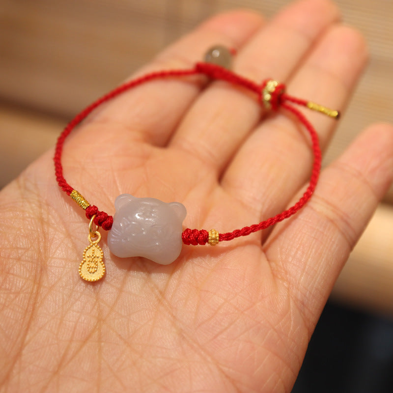 Close-up of a red string bracelet with a small white jade tiger charm held in a hand