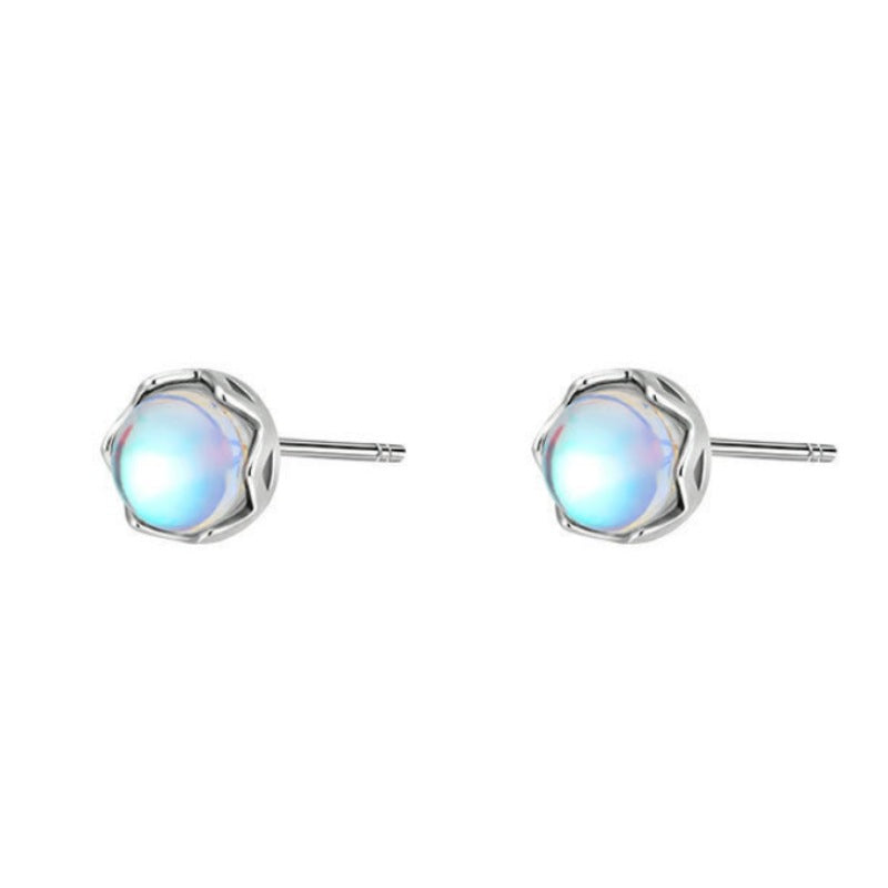 Close up of small round moonstone stud earrings in silver settings on a blue surface