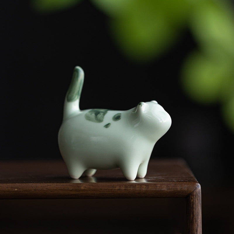 Small white ceramic cat figurine with green spots standing on a wooden surface