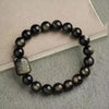 Golden obsidian bracelet with a square carved cat charm resting on a book
