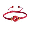 Close-up of a red braided bracelet featuring a round red cinnabar peace buckle charm with gold accents.