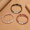 Three bracelets on a brown background showing pink, black, and red cords with geometric charms