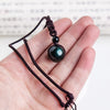 Hand holding a black obsidian pendant necklace with a green sheen