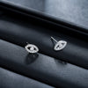 Silver-tone copper stud earrings shaped like an eye with rhinestone details on a black leather surface.