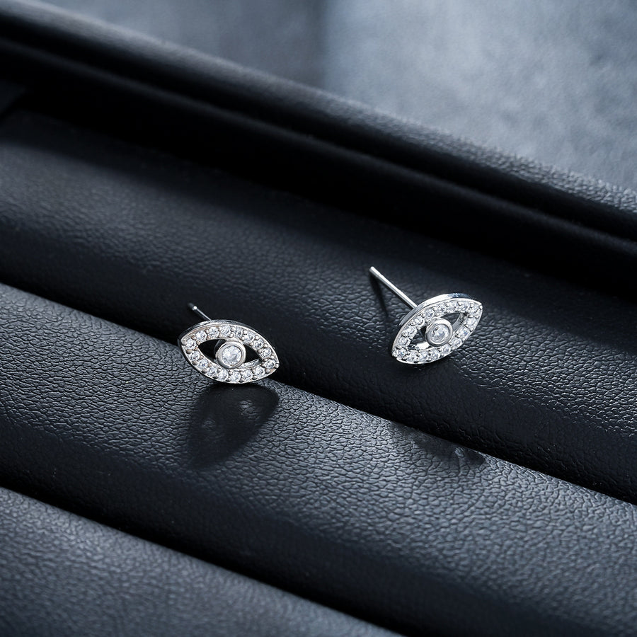 Silver-tone copper stud earrings shaped like an eye with rhinestone details on a black leather surface.