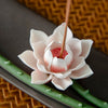 Close up of a pink and white lotus flower ceramic incense holder with a stick burning