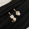 Close up of asymmetric pearl earrings shaped like a cat and a paw on black fabric