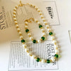 A gold-tone necklace and bracelet featuring white pearls and green glass beads on a white background.