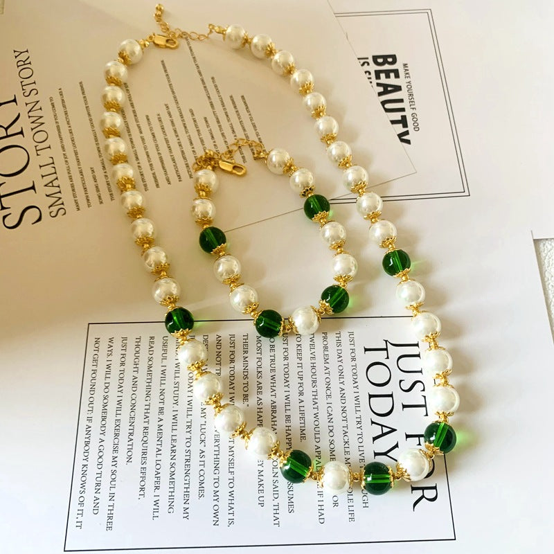 A gold-tone necklace and bracelet featuring white pearls and green glass beads on a white background.