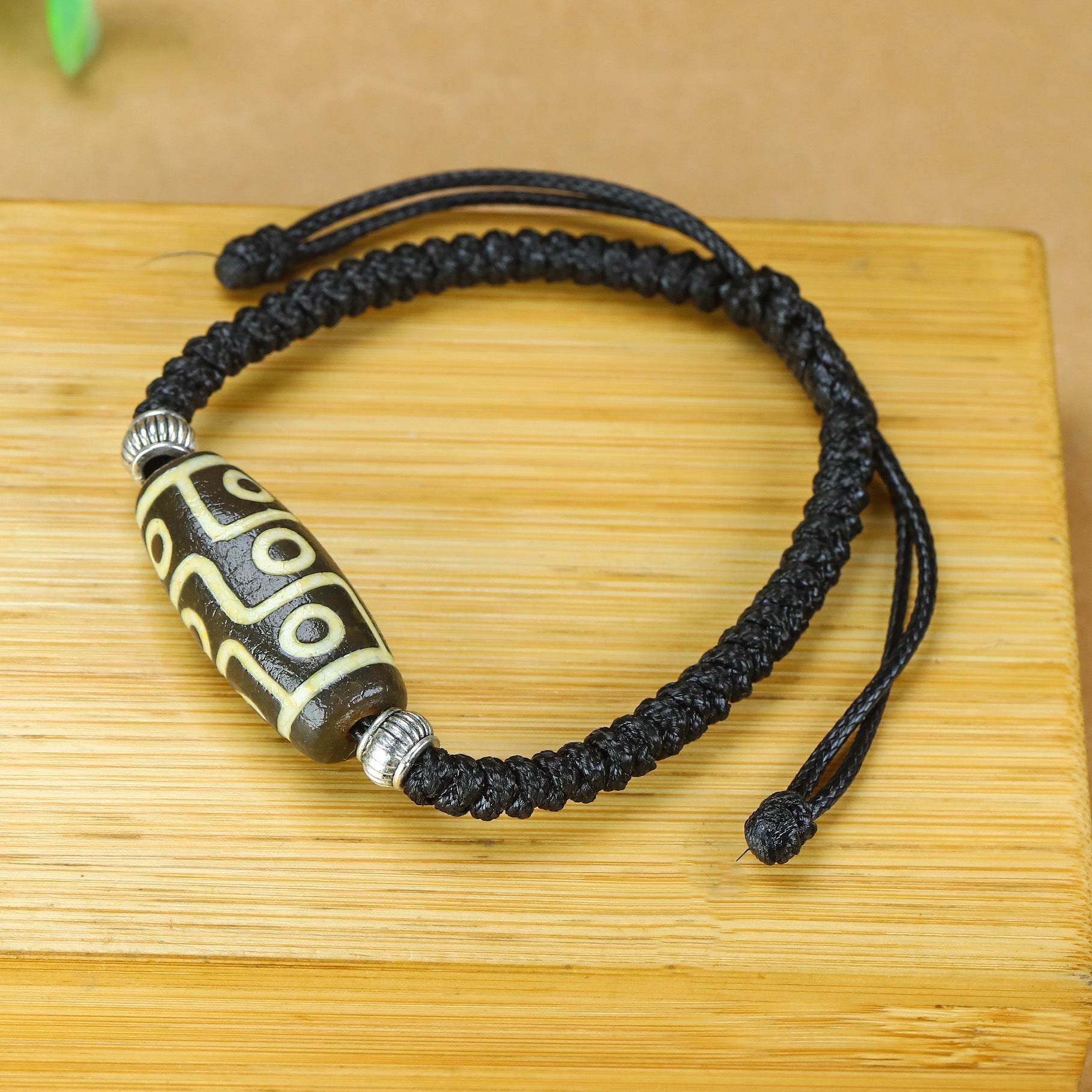 Close-up of a nine-eye Dzi bead bracelet on a black braided cord resting on a wooden surface