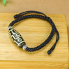 Close-up of a nine-eye Dzi bead bracelet on a black braided cord resting on a wooden surface
