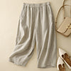 Flat lay of beige linen wide-leg harem pants with elastic waist next to a handbag and shoes