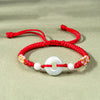 Close up of a red braided bracelet with a white jade peace ring center piece