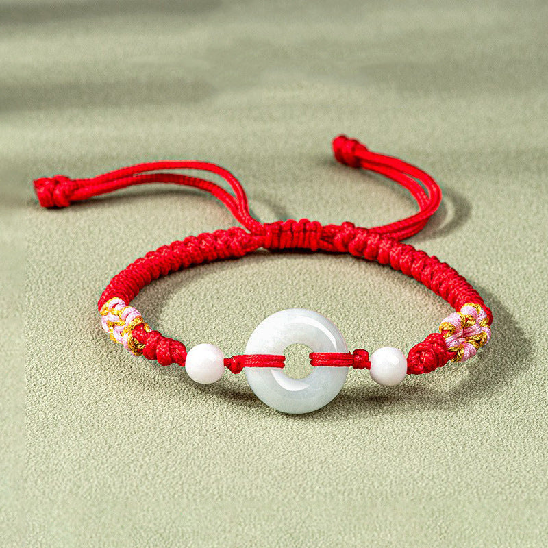Close up of a red braided bracelet with a white jade peace ring center piece