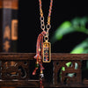 Rectangular gold-tone pendant with colorful thangka art hanging on an irregular metal chain with a red woven tassel.