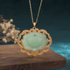 Gold-tone necklace with a green lotus flower pendant resting on wood