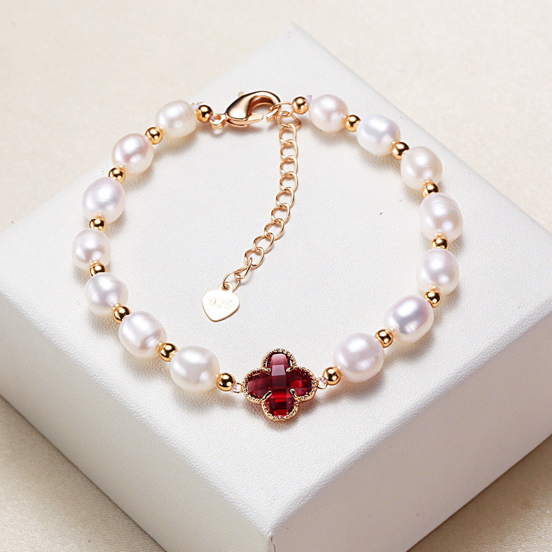 White pearl bracelet with a red four leaf clover charm on a white box
